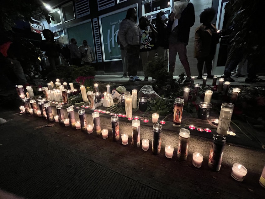 caption: Candles light the sidewalk near The Postman in Seattle's Central District in remembrance of D'Vonne Pickett Jr. Thursday, Oct. 20, 2022. Pickett died a day earlier at a bus stop near his shop on Martin Luther King Jr. Way. 