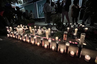 caption: Candles light the sidewalk near The Postman in Seattle's Central District in remembrance of D'Vonne Pickett Jr. Thursday, Oct. 20, 2022. Pickett died a day earlier at a bus stop near his shop on Martin Luther King Jr. Way. 