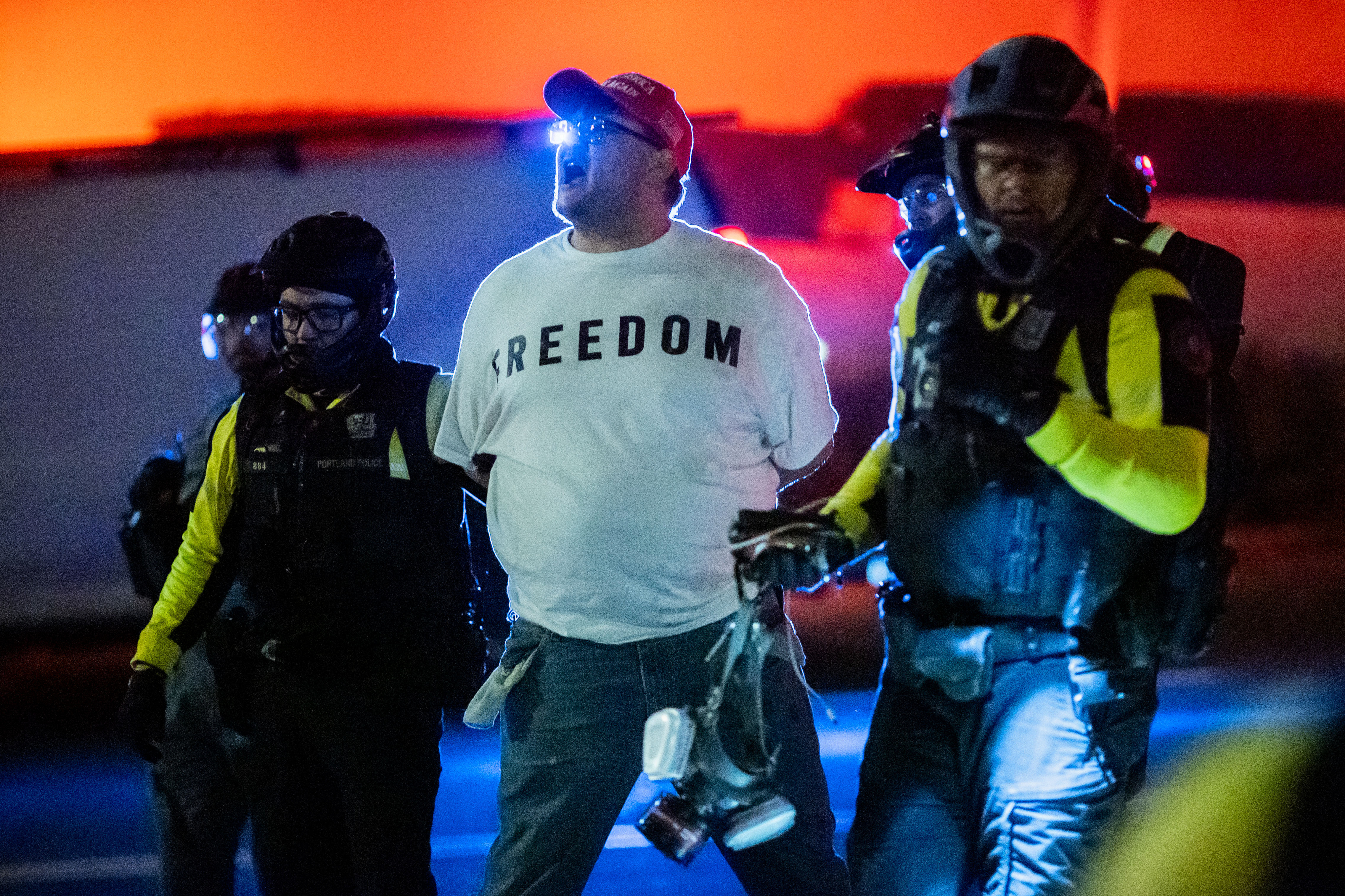 caption: Security officers walk with a man near a U.S. Immigration and Customs Enforcement facility in Portland, Oregon, Sunday, Oct. 5, 2025. 
