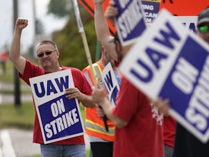 caption: UAW members hold picket signs near a General Motors Assembly Plant in Delta Township, Mich., on Sept. 29, 2023. The UAW is gradually tightening the screws on the Big Three automakers as it pursues new contracts.