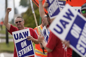 caption: UAW members hold picket signs near a General Motors Assembly Plant in Delta Township, Mich., on Sept. 29, 2023. The UAW is gradually tightening the screws on the Big Three automakers as it pursues new contracts.