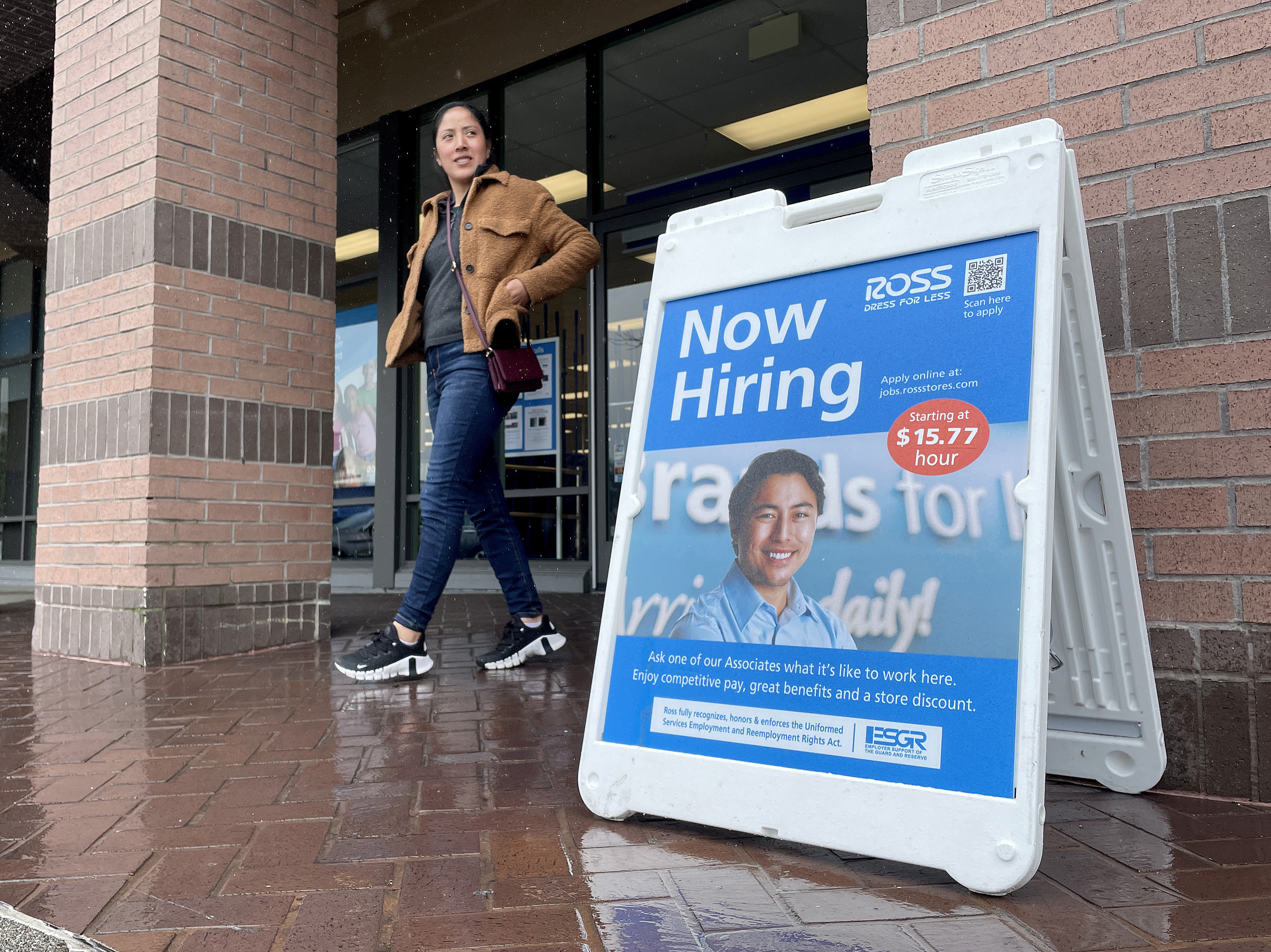 caption: A customer walks by a "now hiring" sign posted in front of a store in Novato, Calif., on April 7, 2023.