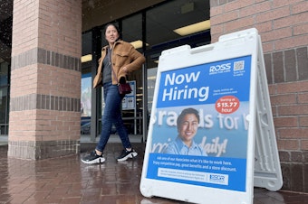 caption: A customer walks by a "now hiring" sign posted in front of a store in Novato, Calif., on April 7, 2023.