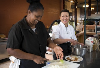 caption: Hiwot Taddesse, left, and Executive Chef Lisa Nakamura laugh while cooking at the Ubuntu Street Cafe on Wednesday, December 13, 2017, in Kent. 