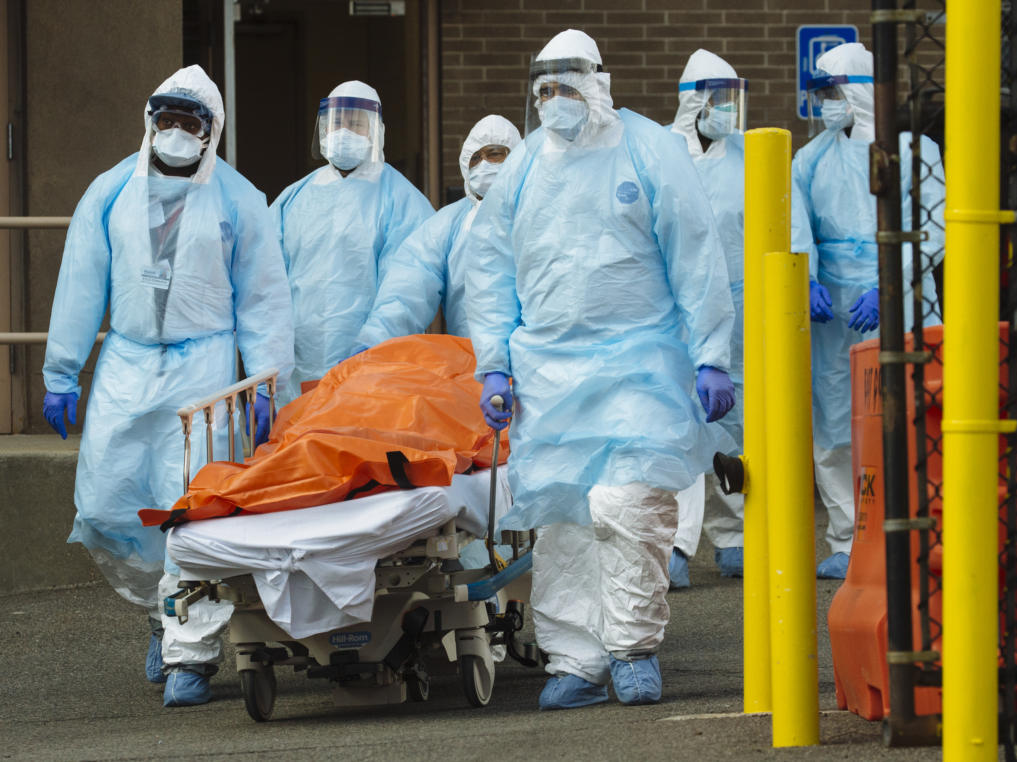 caption: Medical workers in protective clothing move a body to a refrigerated overflow morgue outside the Wyckoff Heights Medical Center in Brooklyn on Thursday.