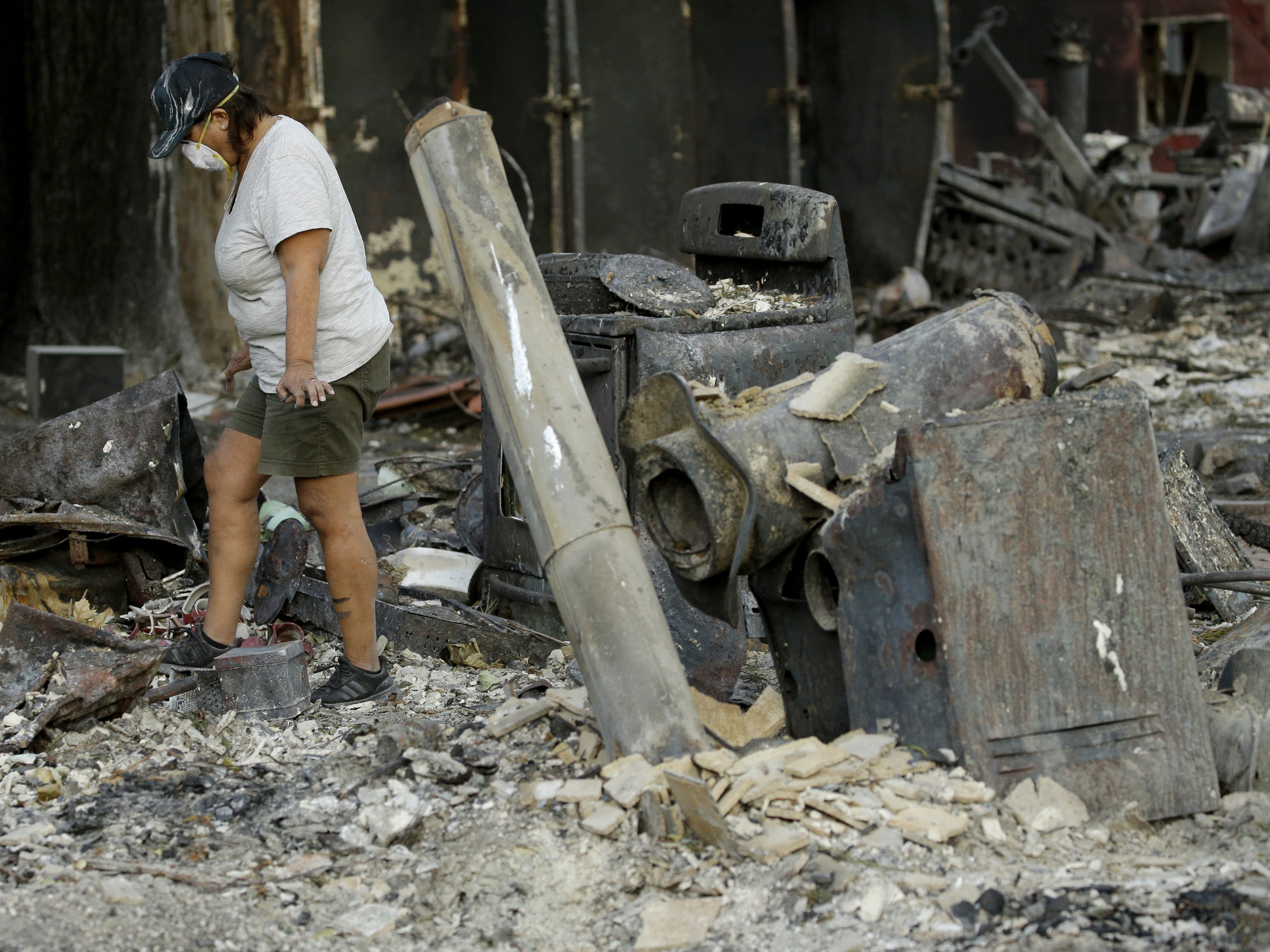 caption: Bernadette Laos looks at what remains of her home, which was destroyed by the Kincade Fire, near Geyserville, Calif.