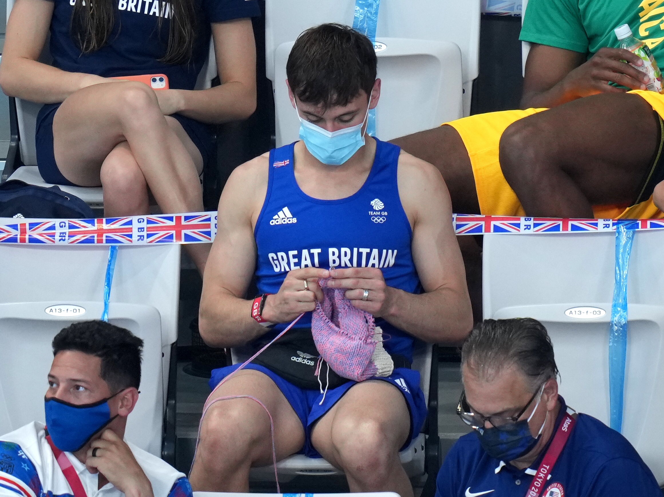 caption: Great Britain's Tom Daley knits in the stands Sunday during the women's 3-meter springboard final at the Tokyo Aquatics Centre at the Olympic Games.