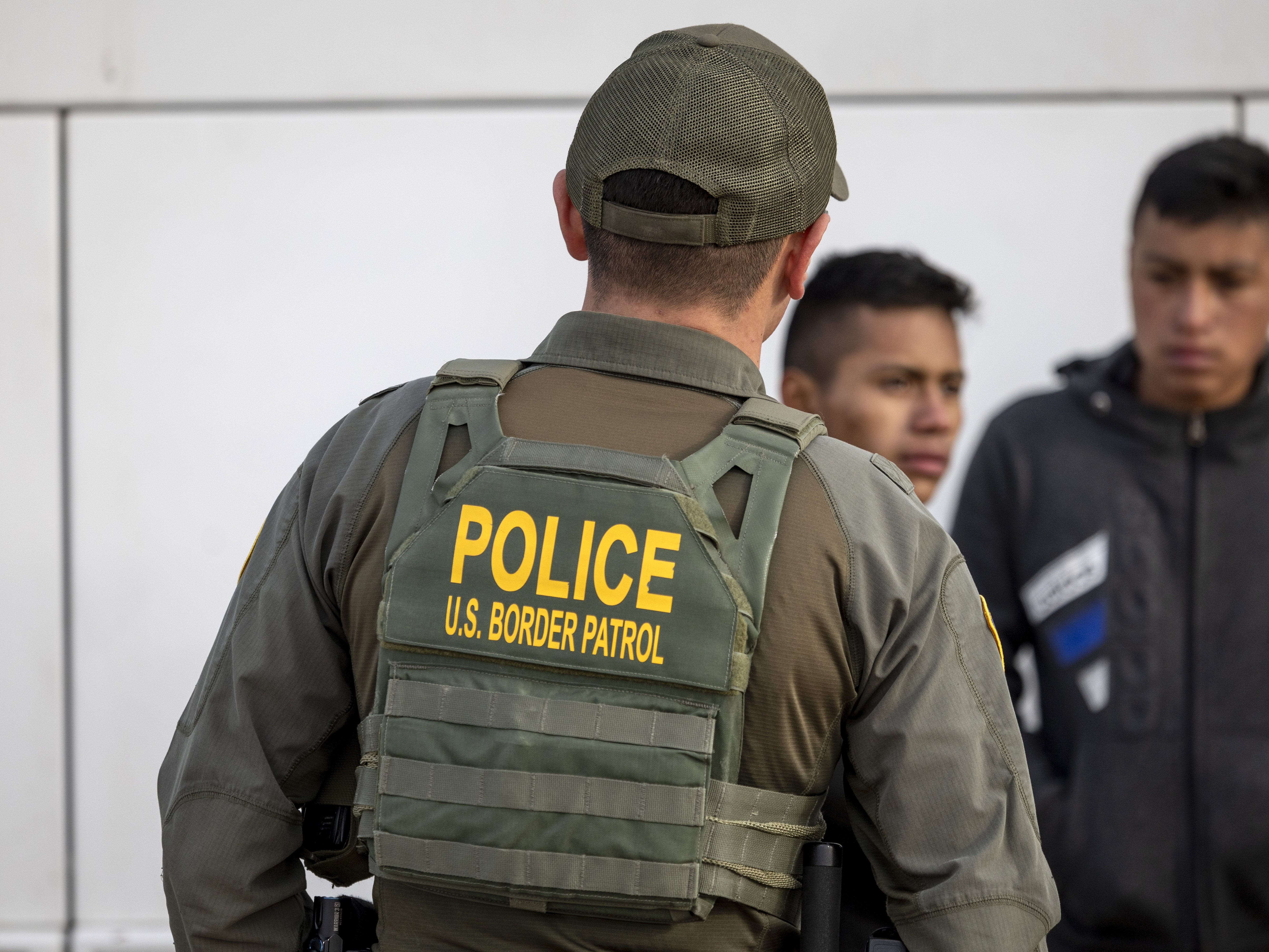 caption: A U.S. Border Patrol agent watches as immigrants prepare to board a bus after crossing the U.S.-Mexico border on Jan. 7, 2024 in Eagle Pass, Texas.