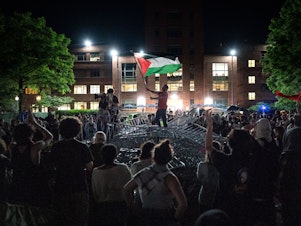 caption: A man holds up a Palestinian flag as activists and students surround piled barricades at an encampment at at George Washington University early Monday.