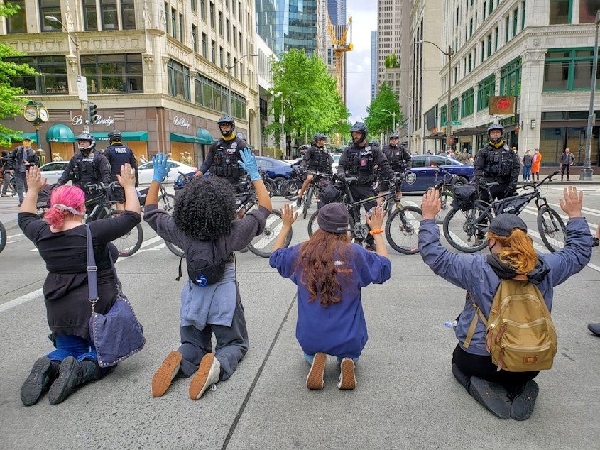 caption: Activists kneel in front Seattle Police during a protest on Sunday, May 31st, 2020.