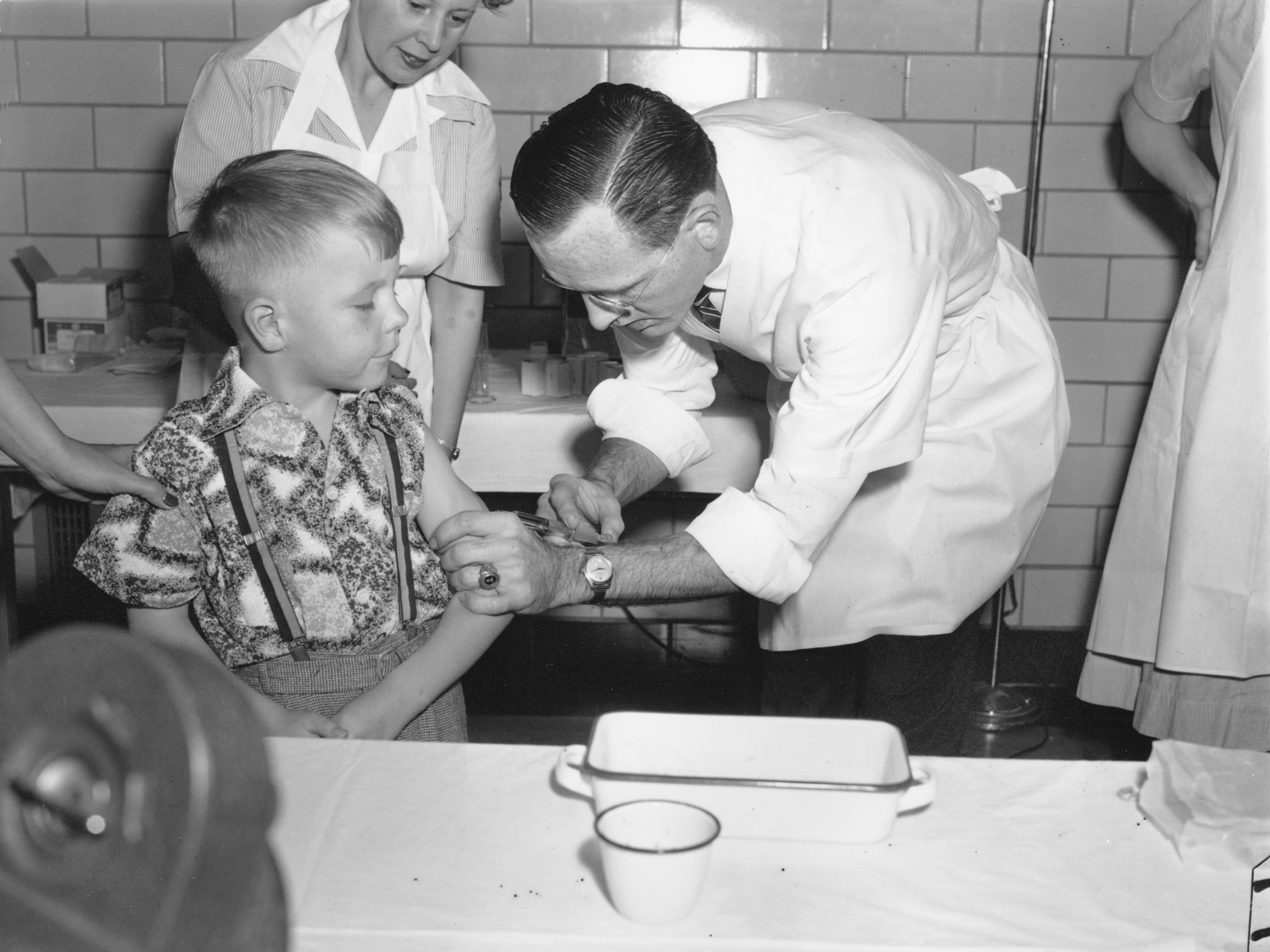 caption: Dr. Richard Mulvaney of Mclean, Va., injects the new polio vaccine into the arm of 6-year-old Randall Kerr, the first of some 100 children to be inoculated on April 26, 1954.