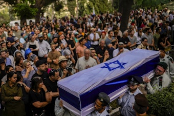 caption: Israeli soldiers carry the flag-covered coffin of a person killed in the Hamas attack earlier this month. Rabbis and reservists have worked around the clock at a military base in Israel to identify and count the dead.