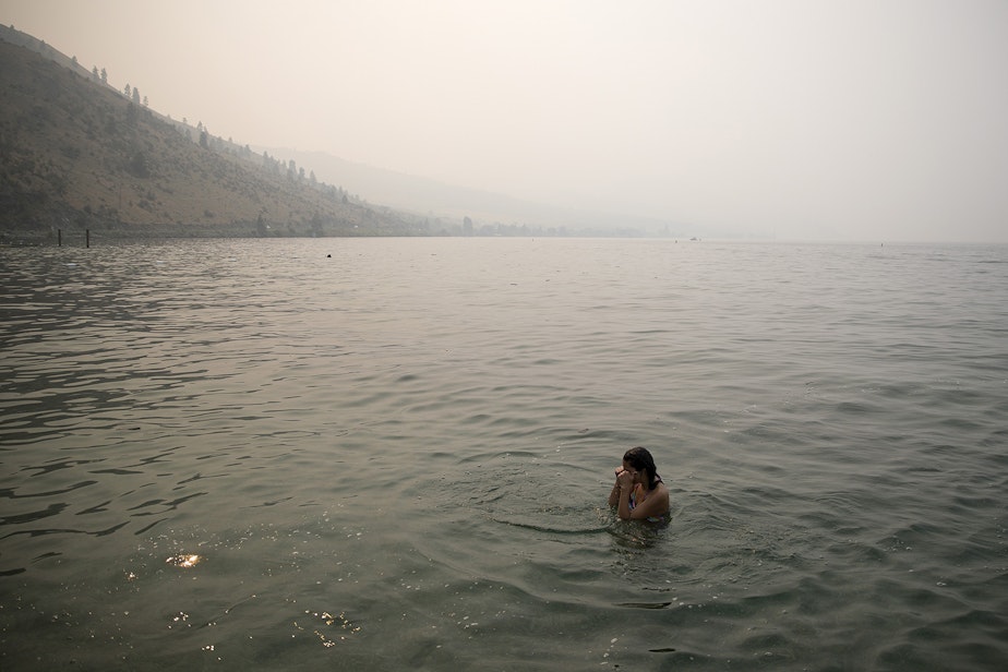 caption: Bellaniy Baltazar, 13, rubs her eyes while swimming amidst heavy smoke from wildfires on Wednesday, August 15, 2018, at Lakeside Park in Chelan. 