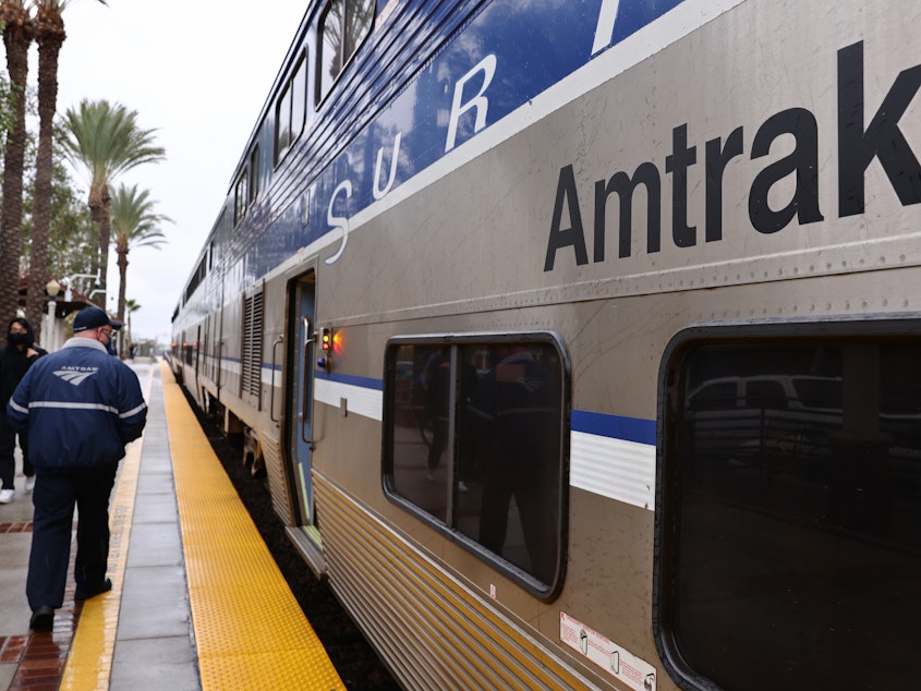 caption: An Amtrak worker and train are pictured on Dec. 9, 2021, in Fullerton, Calif. The company reached a settlement after the Justice Department said Amtrak failed to make stations in its intercity rail transportation system accessible, including to wheelchair users.