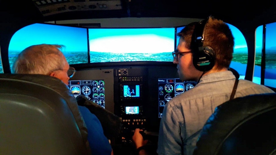 caption: KUOW reporter Casey Martin, right, gets instruction with Spence Campbell of Aviation Training Center on how to use a flight simulator to fly a Bombardier Q400.