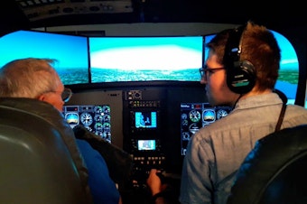 caption: KUOW reporter Casey Martin, right, gets instruction with Spence Campbell of Aviation Training Center on how to use a flight simulator to fly a Bombardier Q400.
