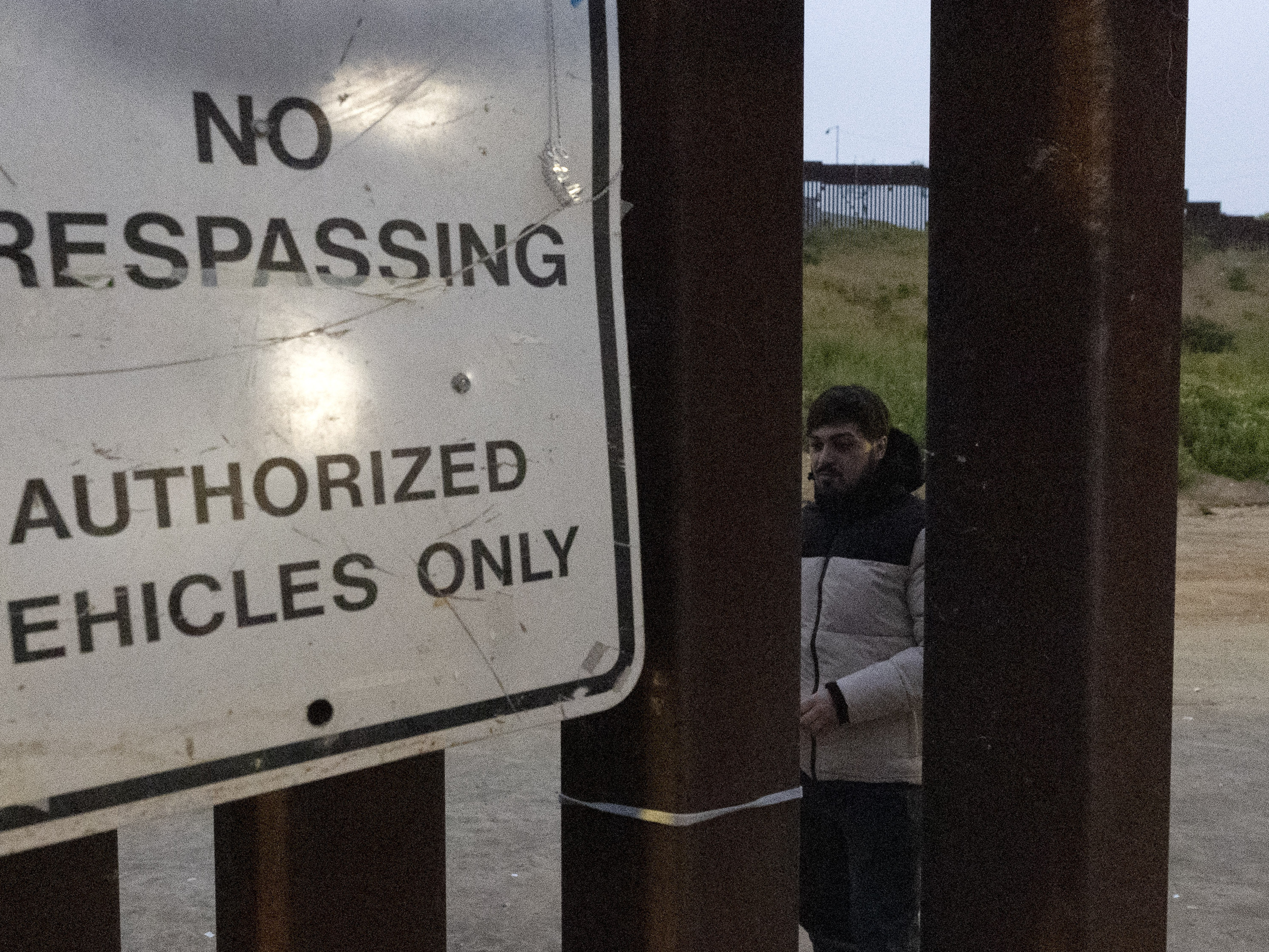 caption: Migrants wait between border walls separating Tijuana, Mexico, and San Diego, to apply for asylum with U.S. authorities, Friday, April 12, 2024, seen from San Diego.