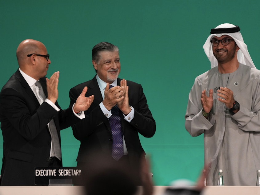 caption: Sultan al-Jaber of the United Arab Emirates, right, celebrates the end of the COP28 climate meeting with United Nations Climate Chief Simon Stiell, left, and COP28 CEO Adnan Amin on Dec. 13, 2023, in Dubai. The final deal included a modest reference to transitioning away from fossil fuels, which scientists say is crucial to avoid catastrophic warming.