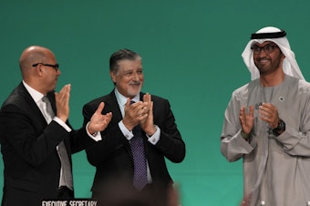 caption: Sultan al-Jaber of the United Arab Emirates, right, celebrates the end of the COP28 climate meeting with United Nations Climate Chief Simon Stiell, left, and COP28 CEO Adnan Amin on Dec. 13, 2023, in Dubai. The final deal included a modest reference to transitioning away from fossil fuels, which scientists say is crucial to avoid catastrophic warming.