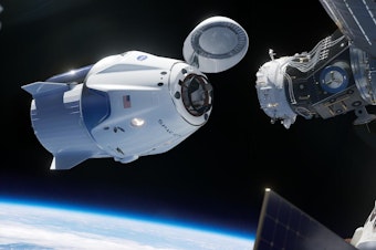 caption: In this illustration, SpaceX's Crew Dragon approaches the International Space Station for docking. The capsule has room to carry seven astronauts.