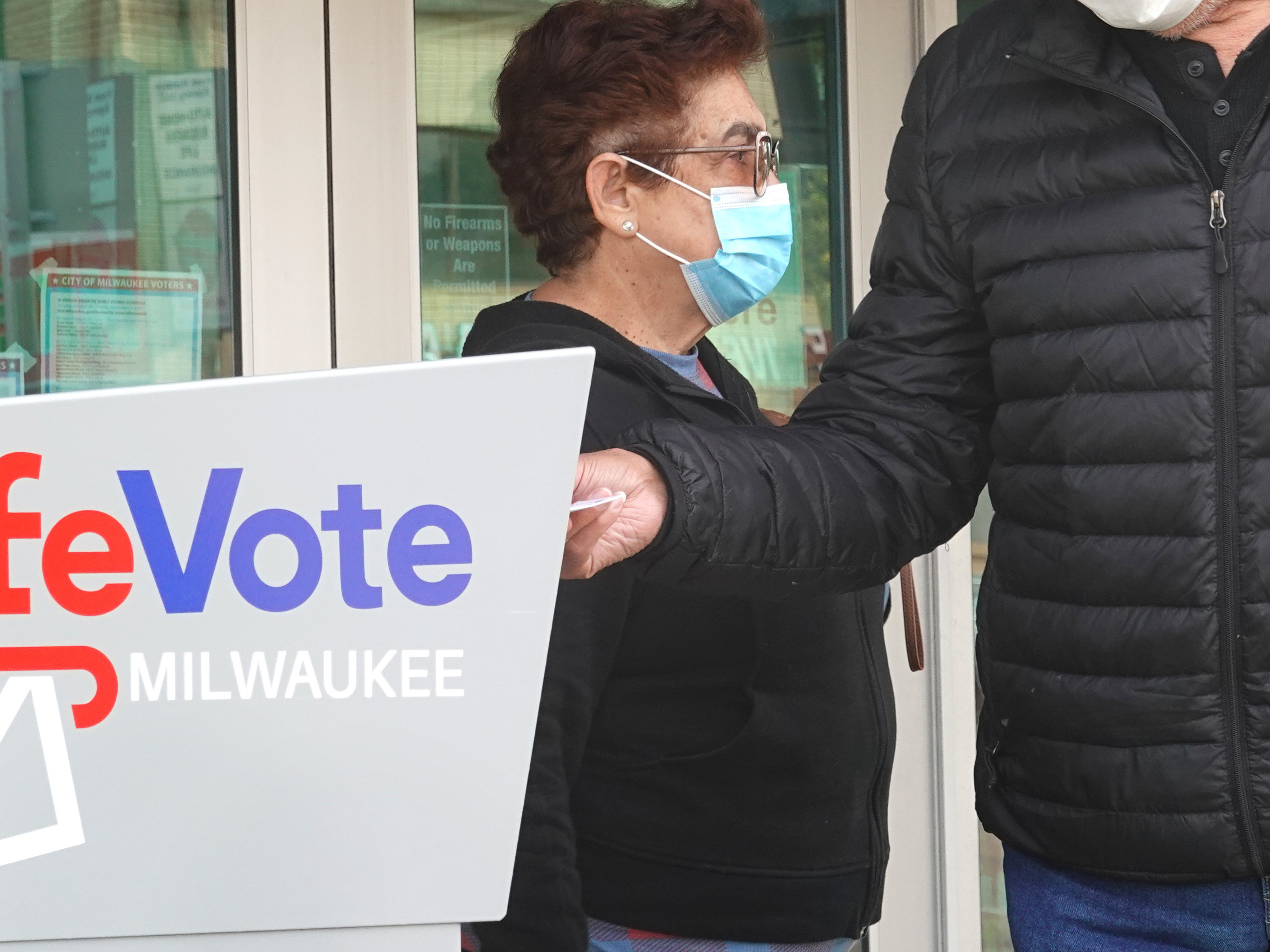 caption: Residents drop mail-in ballots in an official ballot box outside of a Milwaukee library on Oct. 20, 2020.