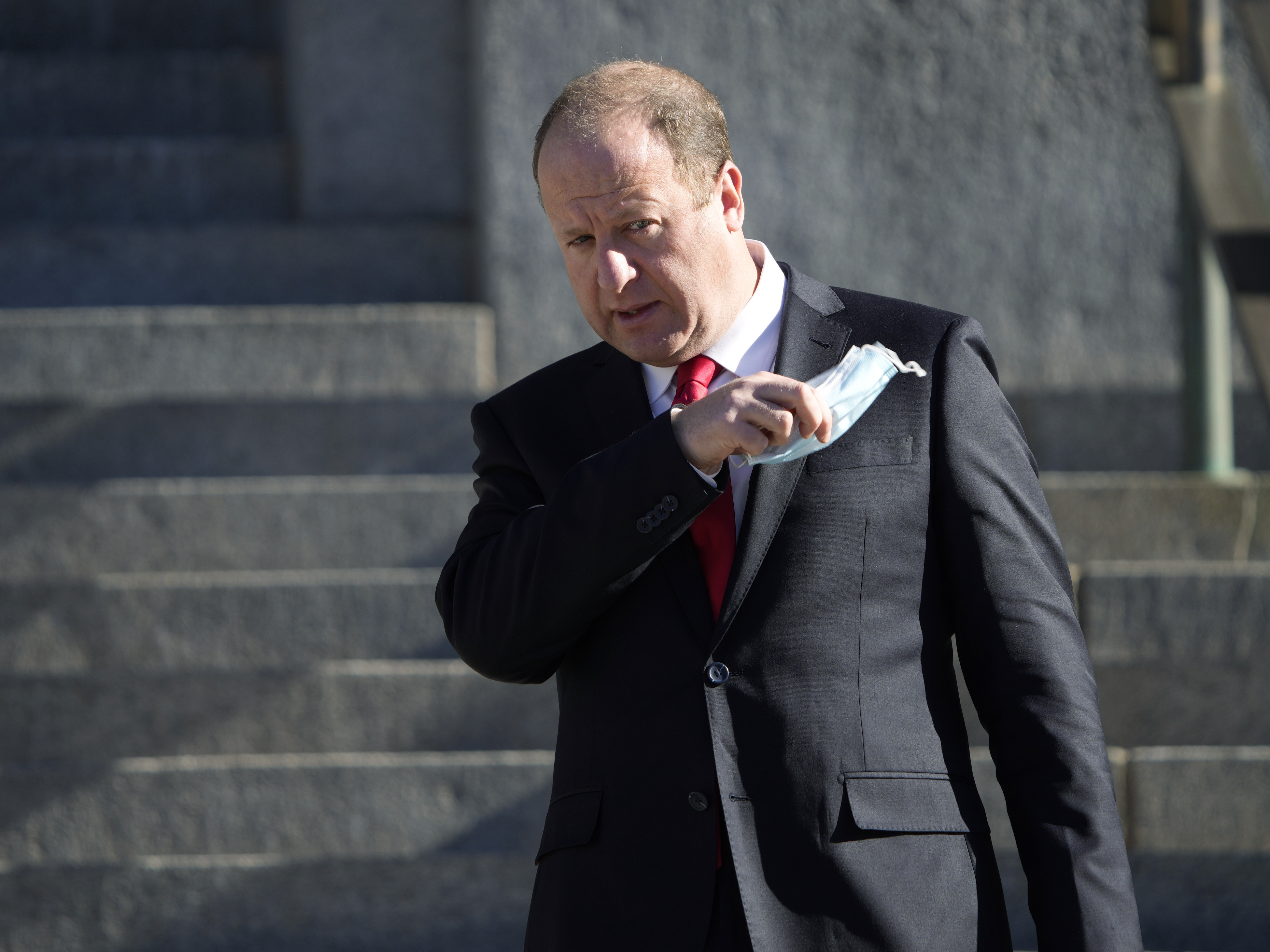 caption: Colorado Gov. Jared Polis pulls off his mask on Jan. 10 in Denver.