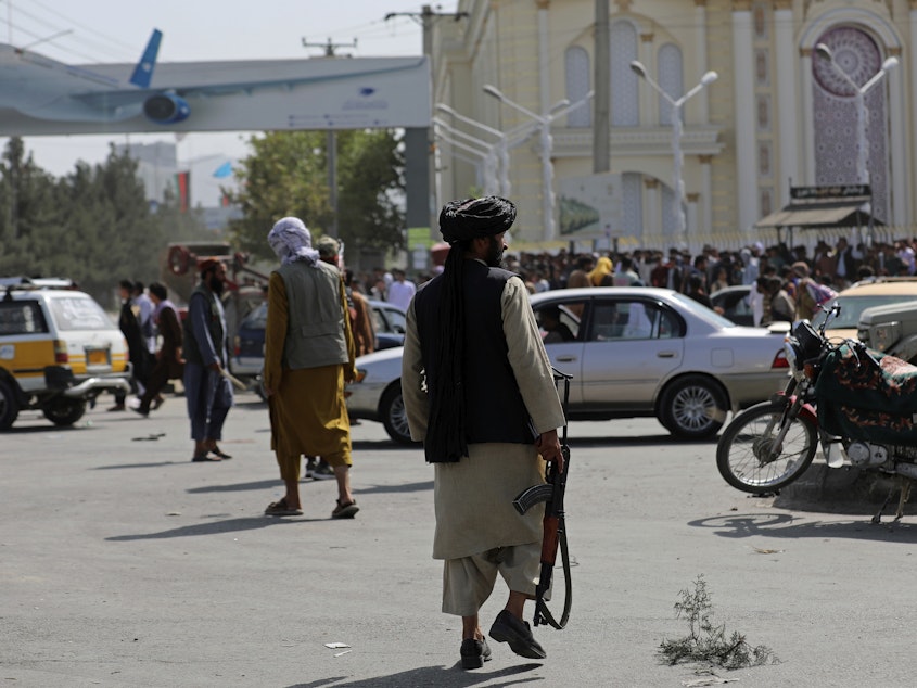 caption: Taliban fighters stand guard in front of the Hamid Karzai International Airport in Kabul, Afghanistan, Monday. Thousands of people packed into the airport, rushing the tarmac and pushing onto planes in desperate attempts to flee the country after the Taliban took over.