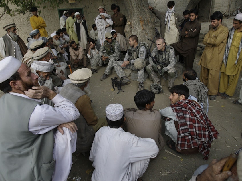 caption: An American lieutenant, center, meets with villagers in Afghanistan's Kunar province in 2009, assisted by an interpreter, sitting to his right wearing a baseball cap. The U.S. will begin the evacuation of some 18,000 Afghan nationals who aided military operations, along with their families, in late July.
