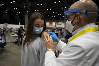 caption: Dr. John L. Thayer, right, applies a bandaid to Olivia Battison's shoulder after administering a Covid-19 vaccine on Saturday, March 13, 2021, at the new civilian-led mass vaccination site at Lumen Field Event Center in Seattle.
