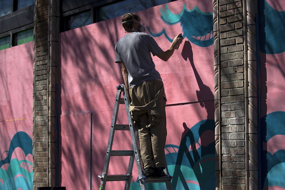 caption: Artist Sam Trout paints a mural on Monday, April 20, 2020, at the intersection of Broadway East and East Harrison Street in Seattle. When complete, the mural will show two astronauts  with the words, "I'll see you when we land."