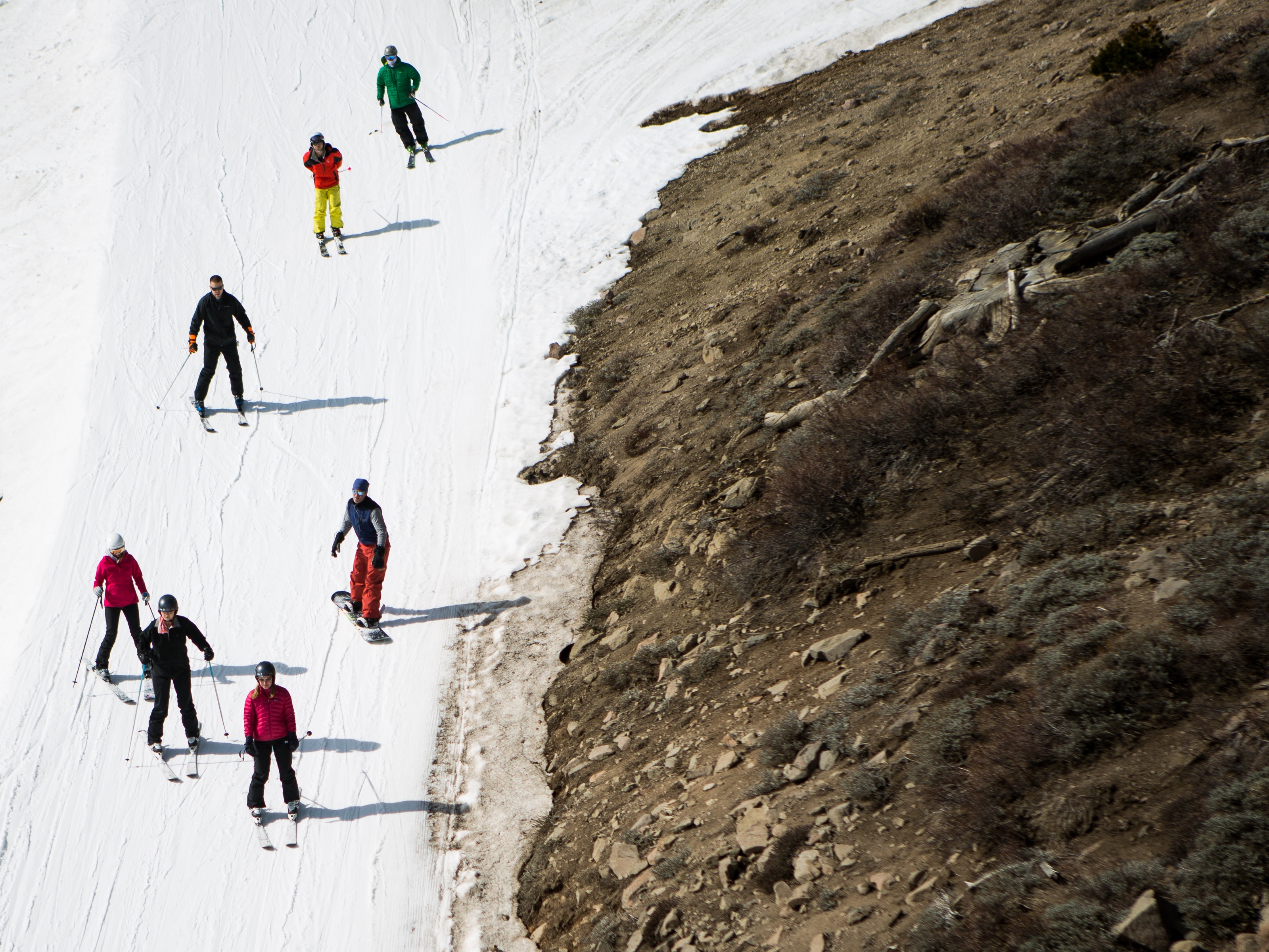 caption: Skiers ski past dry ground at a ski resort in 2015 in Olympic Valley, Calif. The resort changed its name in 2021 and has been among the places removing a derogatory word from their names.