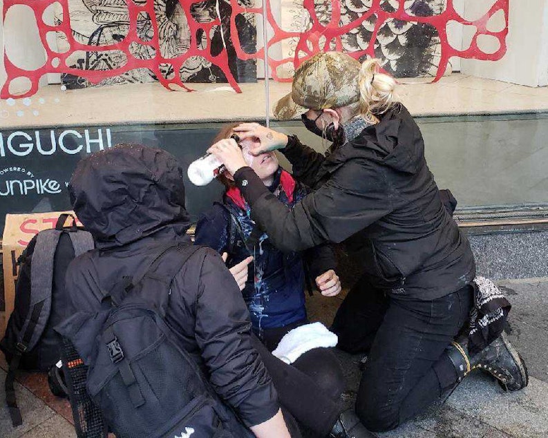 caption: A bystander washes pepper spray from the face of a protester outside the Macy's in downtown Seattle on Saturday, May 30, 2020. Thousands of people were protesting the death in Minneapolis of George Floyd at the hands of police.