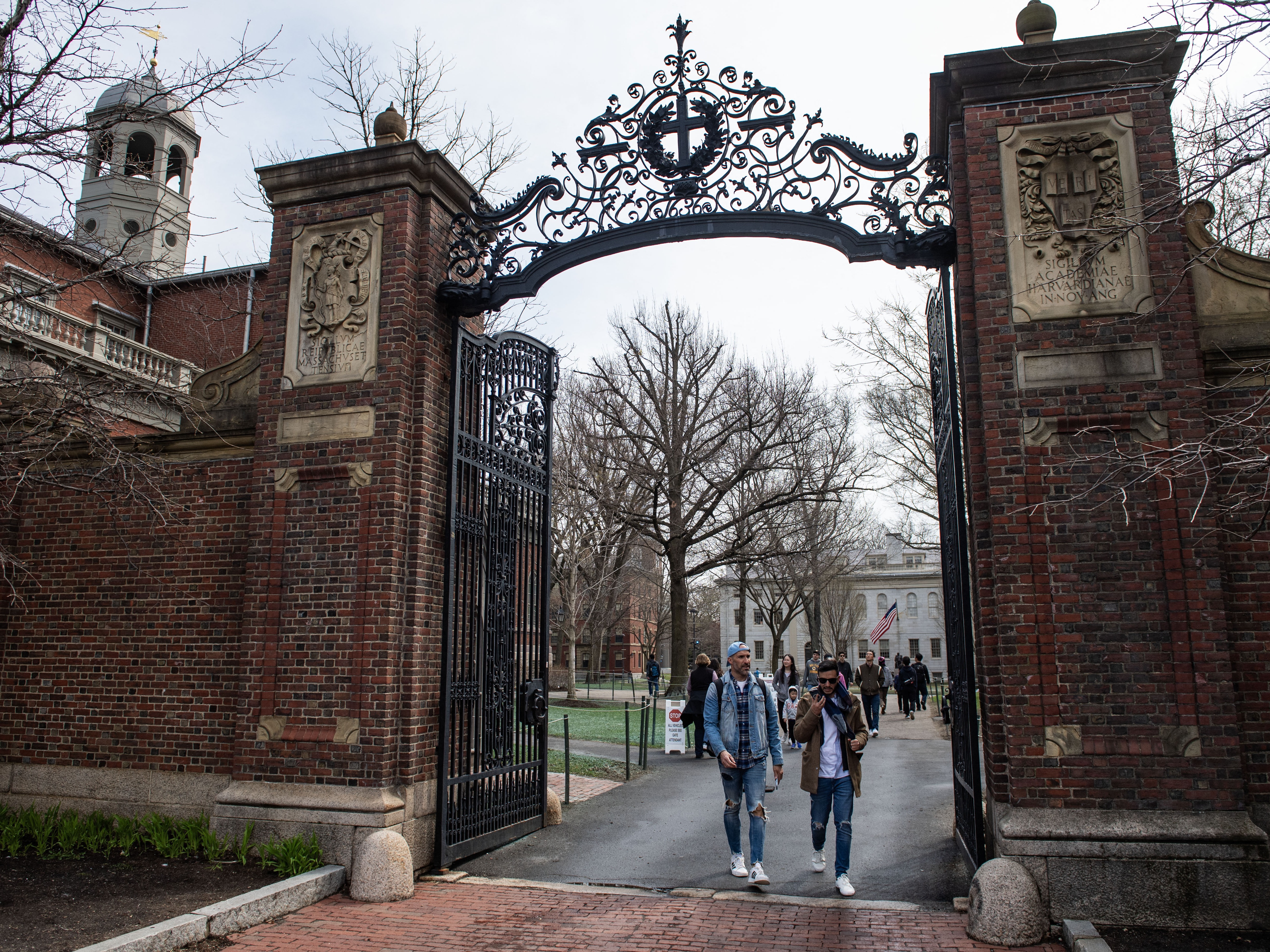caption: People walk through a gate as they exit Harvard Yard on the campus of Harvard University  in Cambridge, Mass.