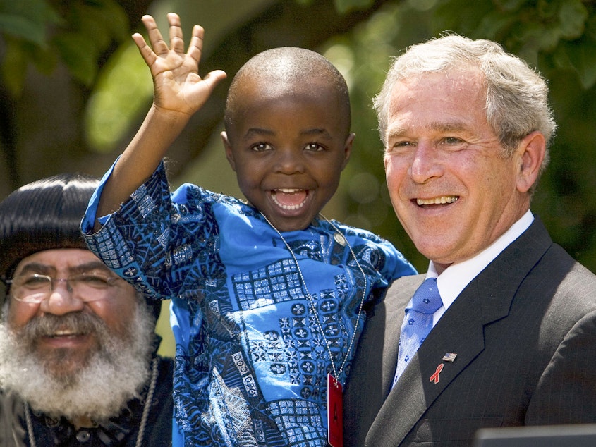 caption: In 2003, President George W. Bush created PEPFAR to help countries tackle the HIV/AIDS crisis. Four years later, he spoke at the Rose Garden to urge lawmakers to set aside $30 billion for the cause over the next 5 years. Joining him were Kunene Tantoh of South Africa and her 4-year-old son (pictured). Tantoh, who is HIV-positive, coordinated a U.S.-funded mentoring program for mothers with HIV.