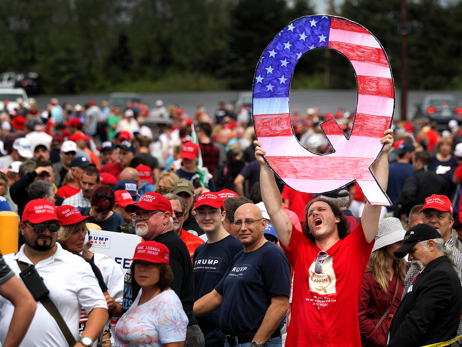 caption: David Reinert holds up a large "Q" sign that represents QAnon while waiting in line to see then-President Donald Trump at his rally in Wilkes Barre, Pa., on Aug. 2, 2018.