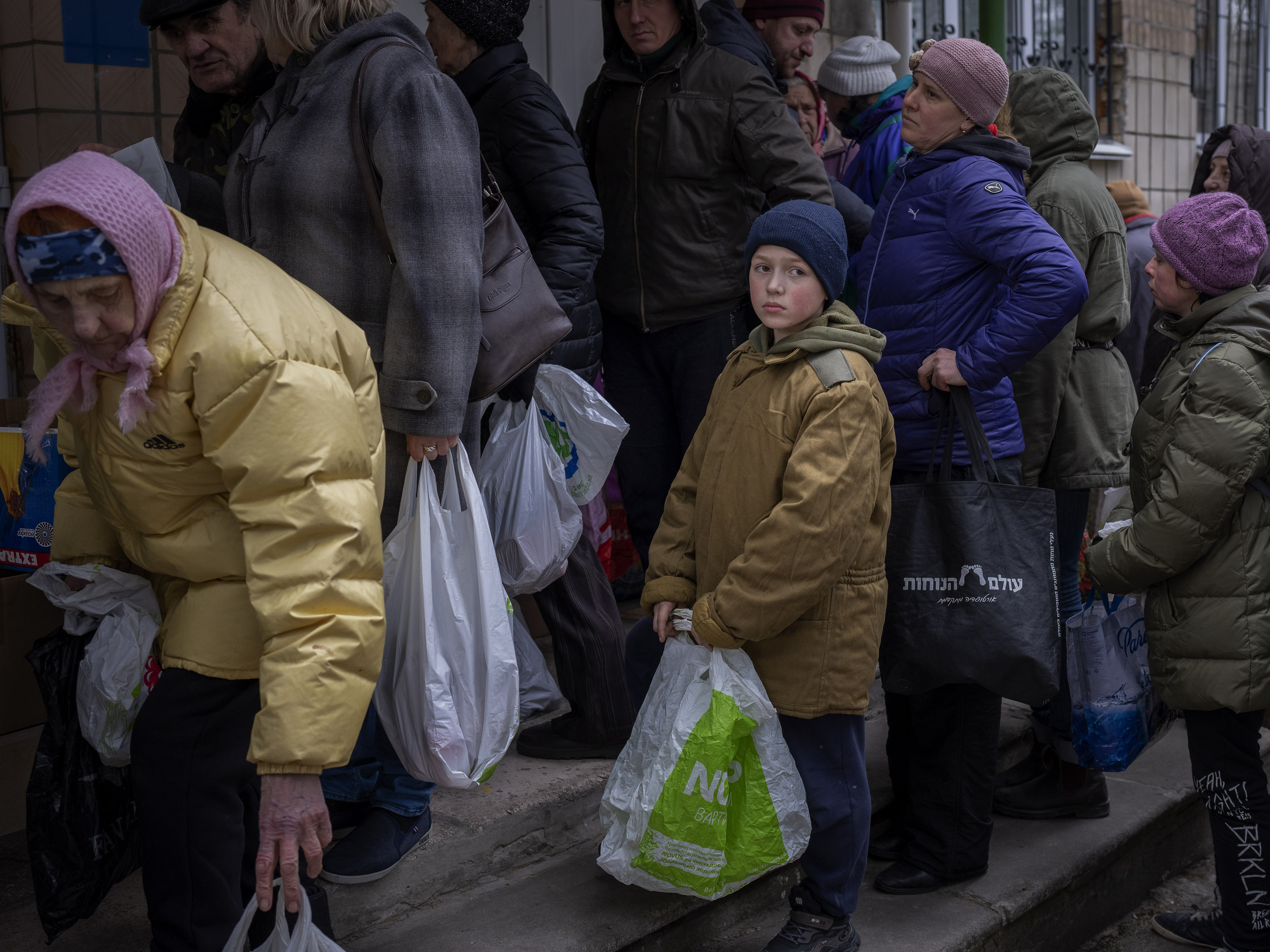 caption: Sergei, 11, waits his turn to receive donated food during an aid humanitarian distribution in Bucha, in the outskirts of Kyiv, on Tuesday, April 19, 2022.