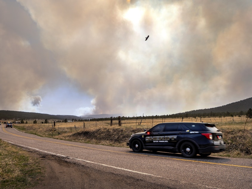 caption: San Miguel County Sheriff's Officers patrol N.M. 94 near Penasco Blanco, N.M., as the Calf Fire burns nearby on Friday.