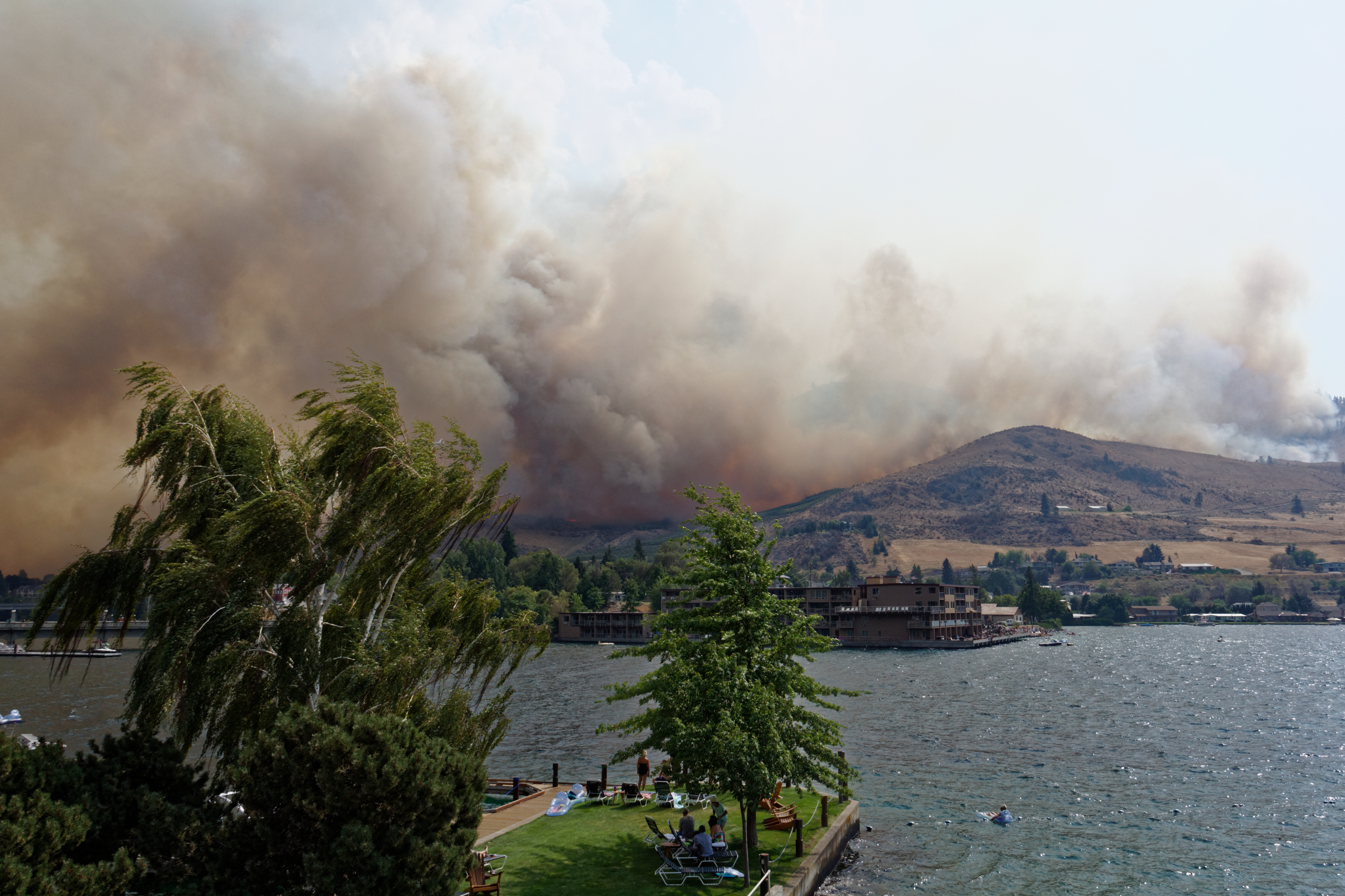 caption: Beachgoers in Chelan watch as the wildfire comes over the butte.