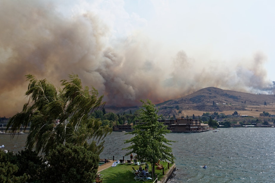 caption: Beachgoers in Chelan watch as the wildfire comes over the butte.