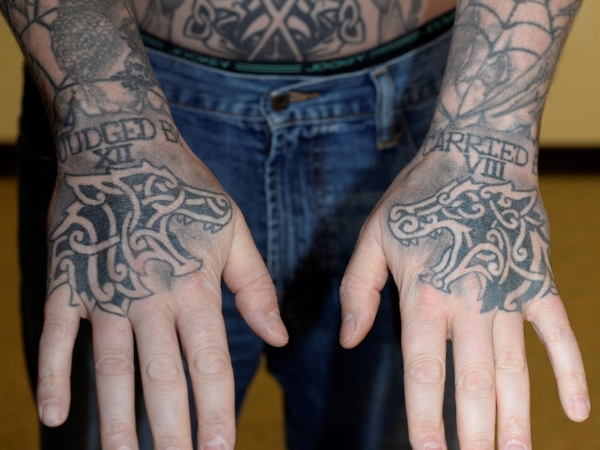 caption: Auburn police officer Jeffrey Nelson displays tattoos on his hands: “JUDGED BY XII” on the right hand. “CARRIED BY VIII” on the left. That’s shorthand for an old policing proverb: “I’d rather be judged by 12” jurors than “carried by six” — or sometimes eight — pallbearers.