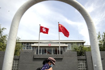 caption: A woman wearing a face mask walks by the Government of Hong Kong Special Administrative Region office building in Beijing in June following the imposition of a national security law on Hong Kong. Ten Hong Kong fugitives were sentenced to prison Wednesday for illegally crossing international boundaries.