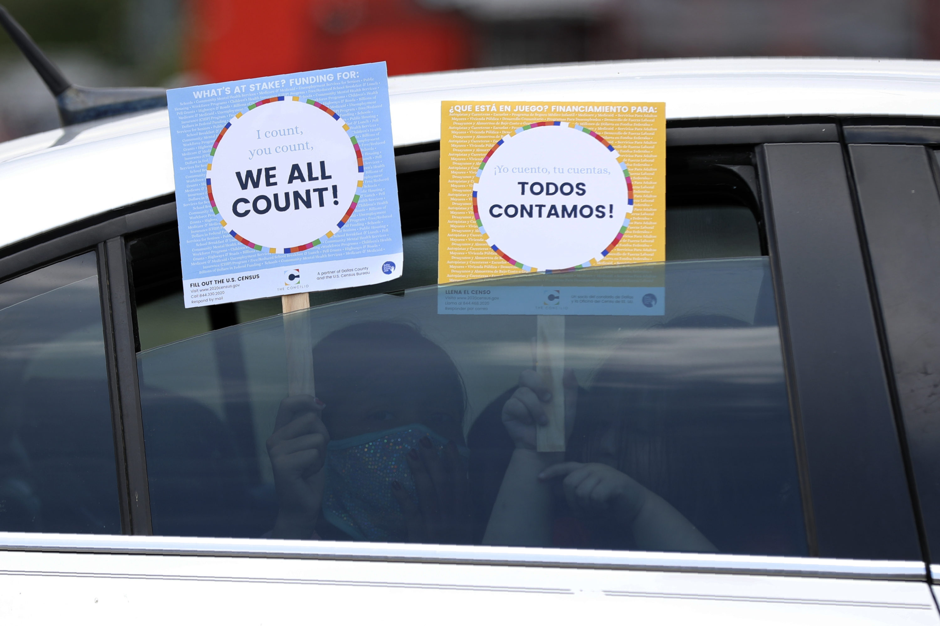 caption: In this June 25, 2020, file photo, two young children hold signs through the car window that make reference to the 2020 U.S. Census as they wait in the car with their family at an outreach event in Dallas. (Tony Gutierrez/AP Photo)