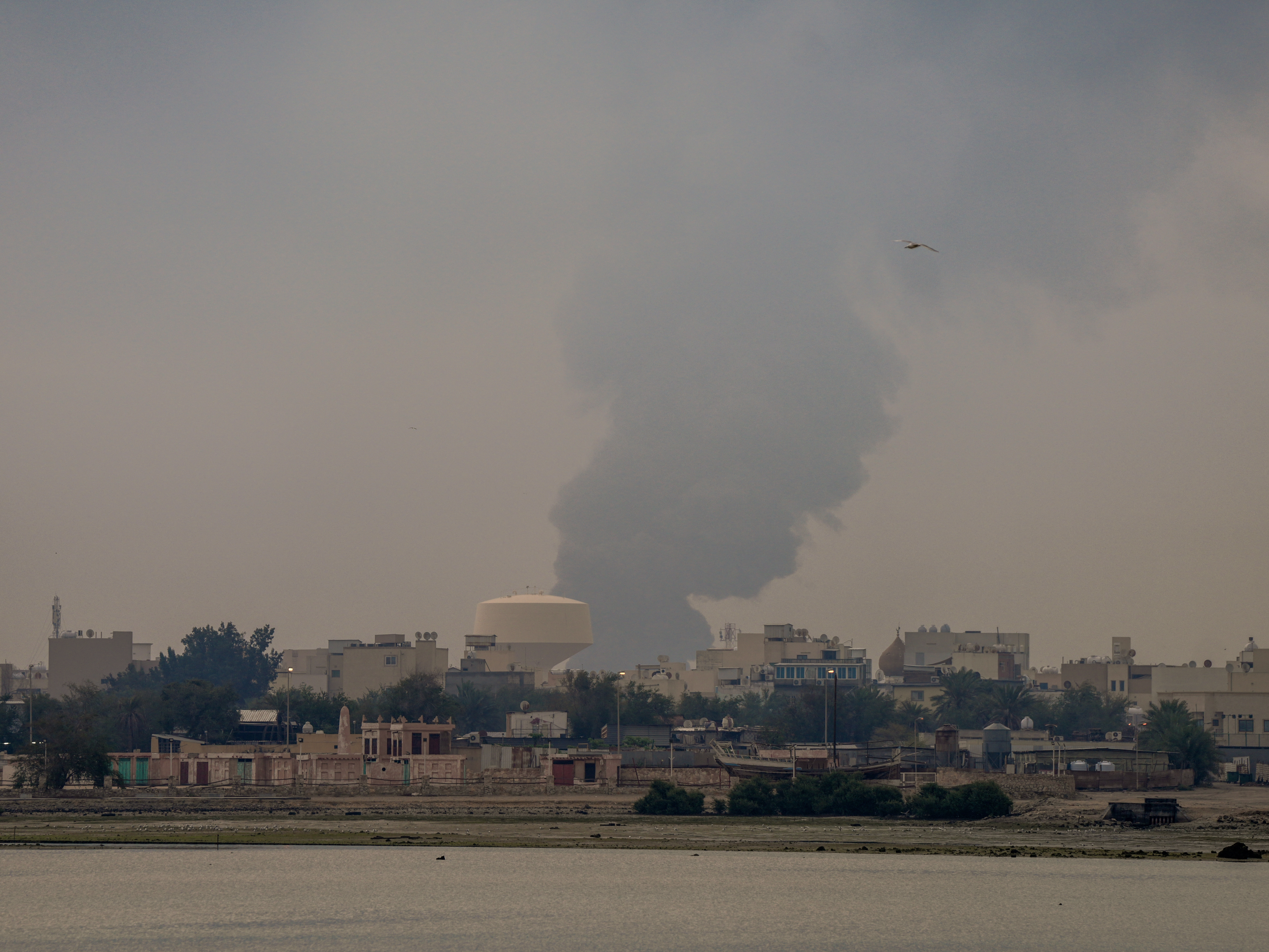 caption: A plume of smoke rises after a reported Iranian strike on fuel tanks in Muharraq, Bahrain, on March 12.