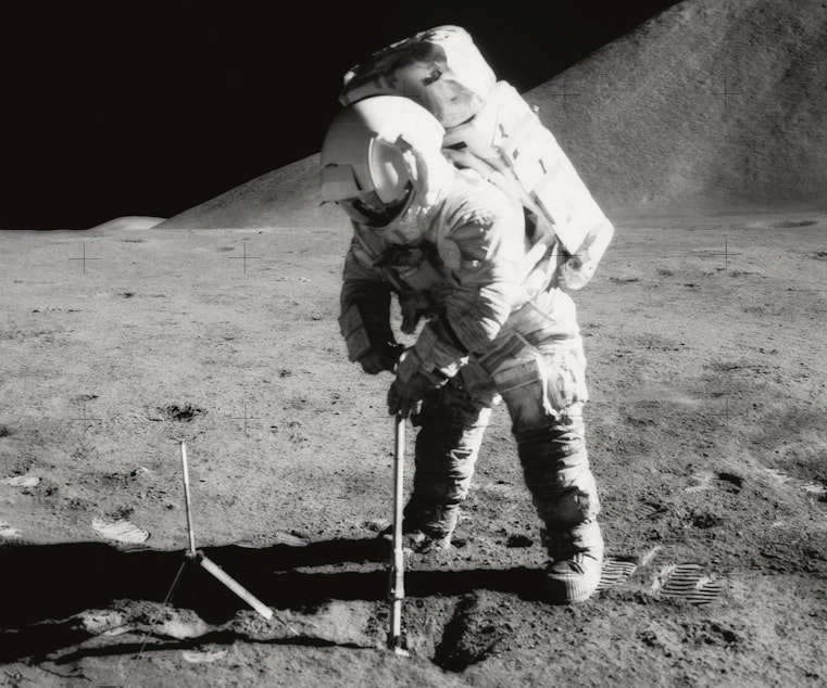 caption: Astronaut James B. Irwin, lunar module pilot, uses a scoop in making a trench in the lunar soil during Apollo 15 extravehicular activity (EVA). Irwin had a heart attack while orbiting the moon, which made NASA realize that they needed a better health monitoring system.