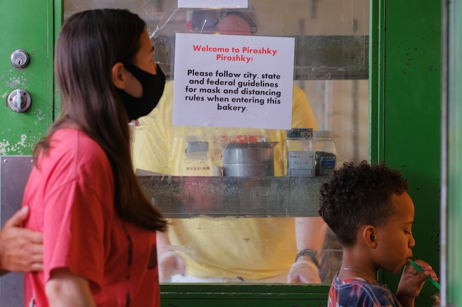 caption: A sign posted at Piroshky Piroshky! in Pike Place Market encourages patrons to follow local guidelines for masking and distancing, August 3, 2021. Some patrons chose to mask while inside, some did not.