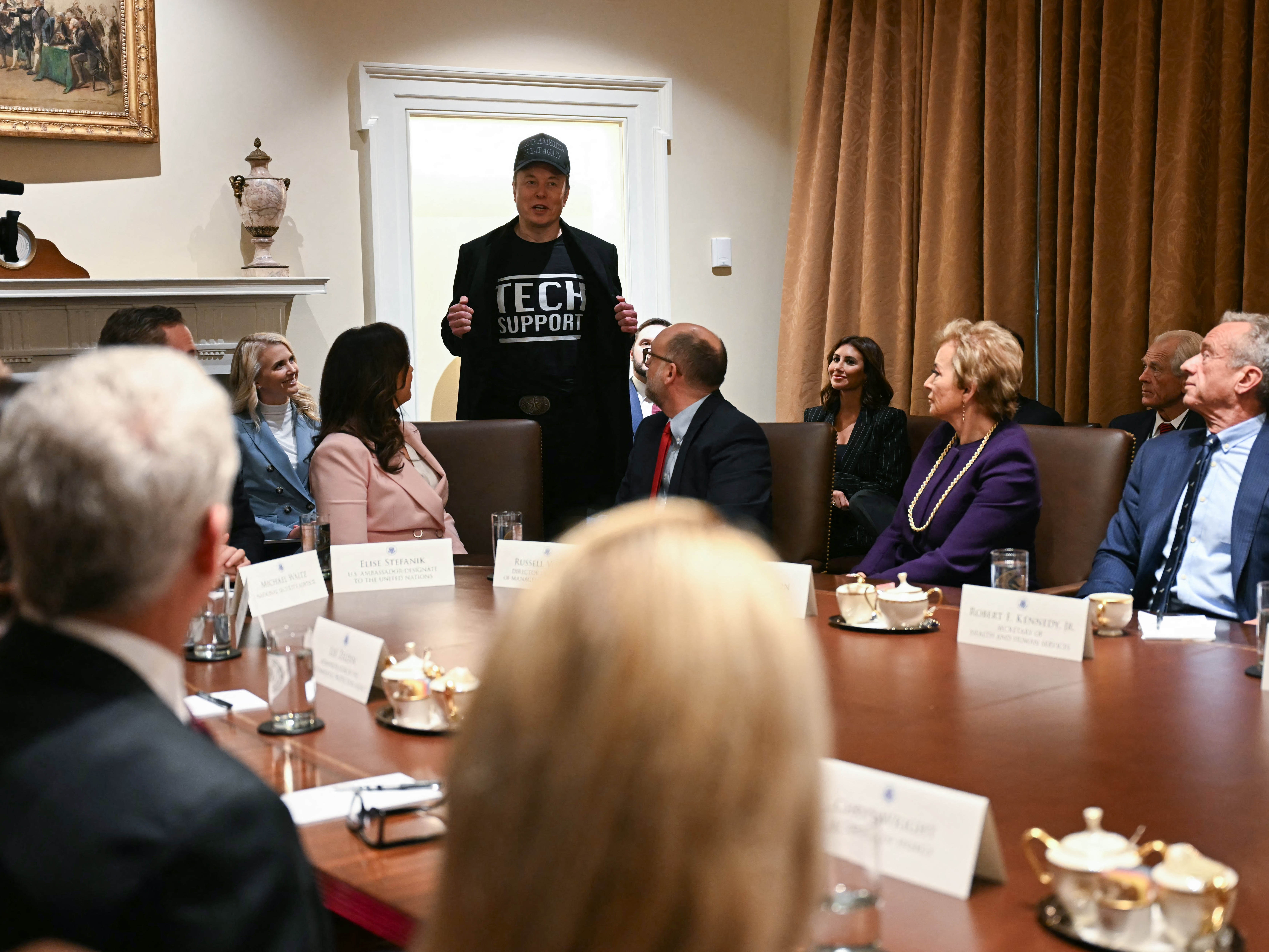 caption: Elon Musk, who oversees the Trump administration's Department of Government Efficiency, wears a shirt that says "Tech Support" as he speaks during President Trump's Cabinet meeting Wednesday at the White House.