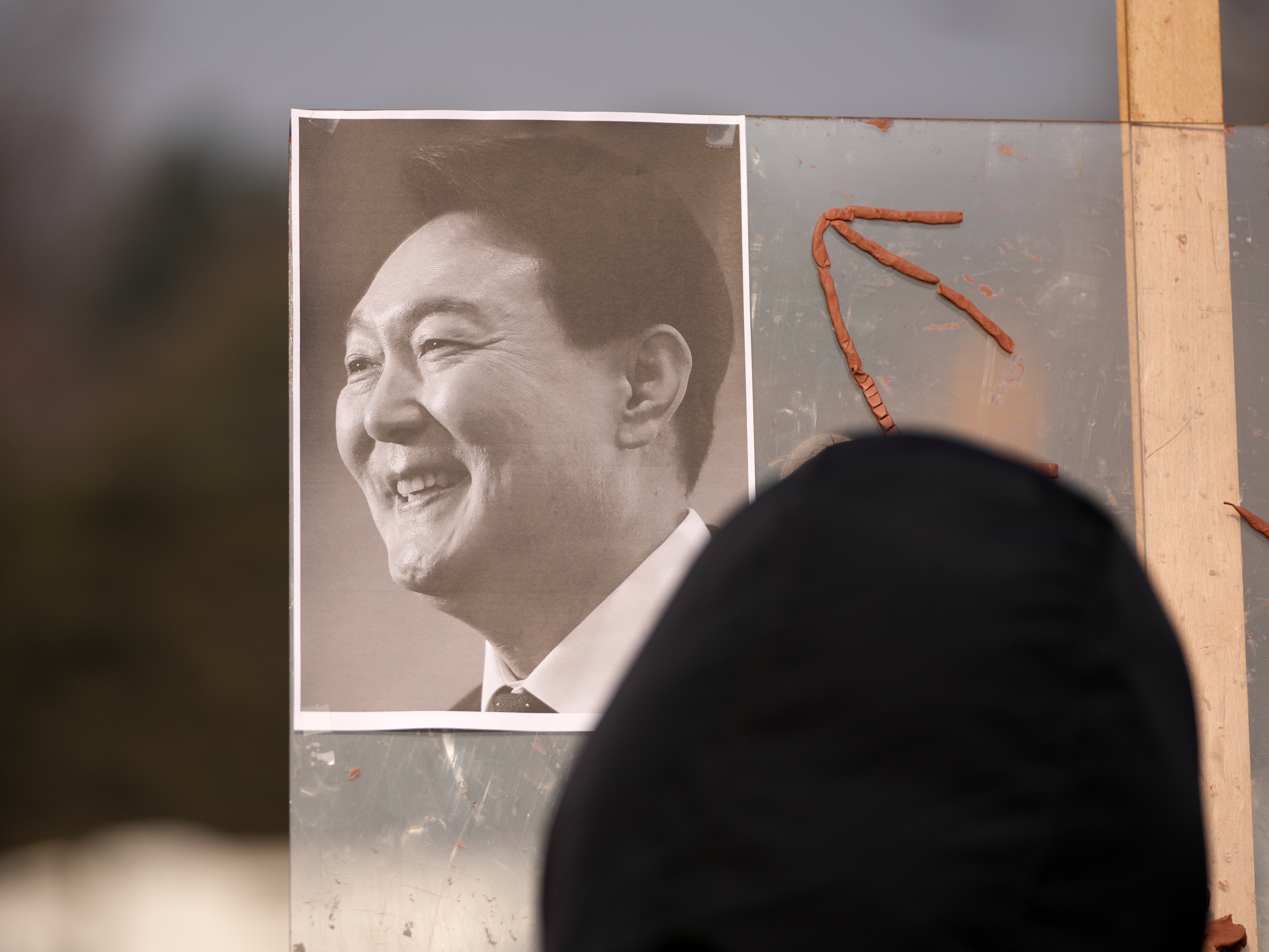 caption: A picture of former South Korean President Yoon Suk Yeol is placed on a board as supporters gather outside Seoul Central District Court, in Seoul, South Korea, Friday, Jan. 16, 2026.
