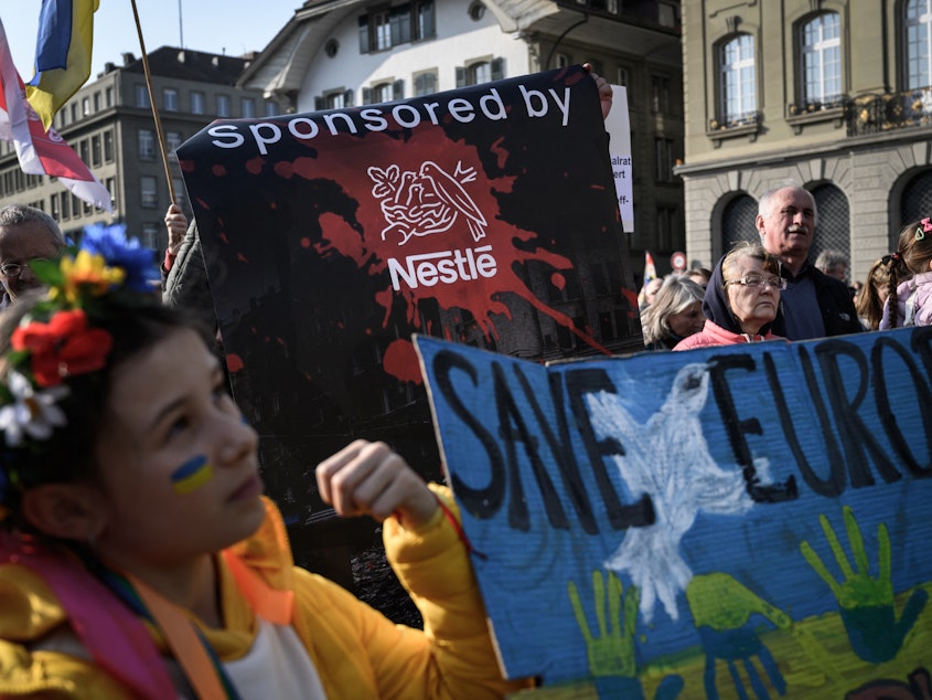 caption: Protesters hold a banner calling out Swiss food giant Nestlé during a demonstration against the Russian invasion of Ukraine next to the Swiss House of Parliament in Bern on Saturday. The company faced criticism in recent days for continuing to do busines in Russia.