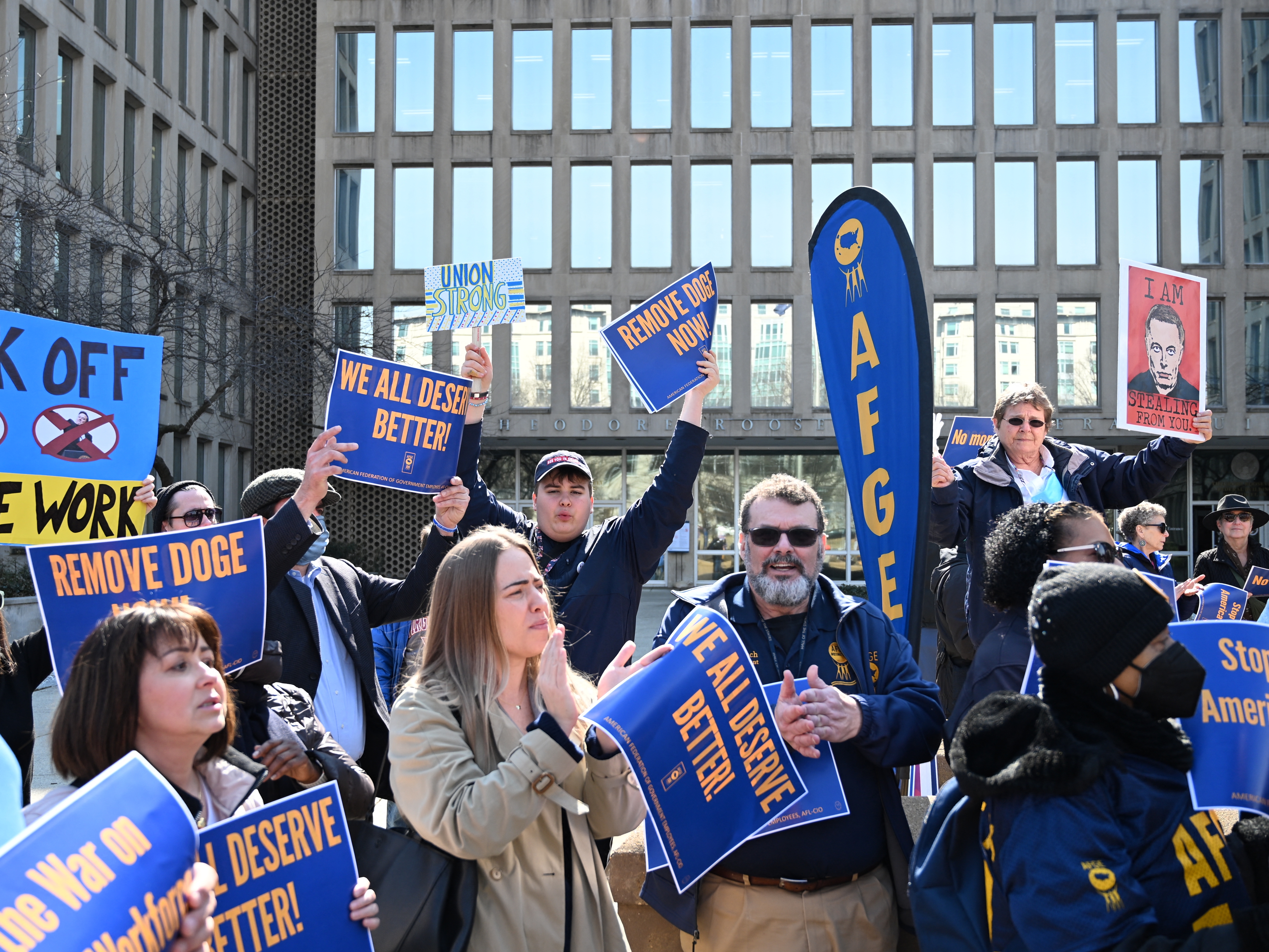 caption: Protesters hold signs in solidarity with the American Federation of Government Employees at a March 4 rally in support of federal workers at the Office of Personnel Management in Washington, D.C.