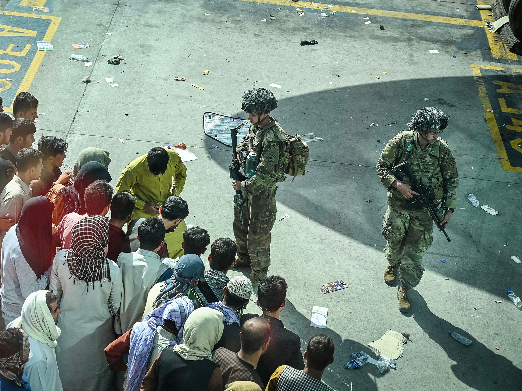 caption: U.S. soldiers stand guard as Afghan people wait at the Kabul airport in Kabul on Aug. 16, 2021, after a stunningly swift end to Afghanistan's 20-year war, as thousands of people mobbed the city's airport trying to flee the group's feared hardline brand of Islamist rule.